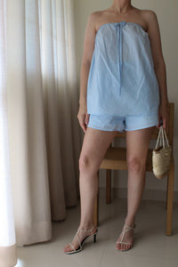 Person sitting on a chair with a light blue skirt and sandals in a neutral setting.